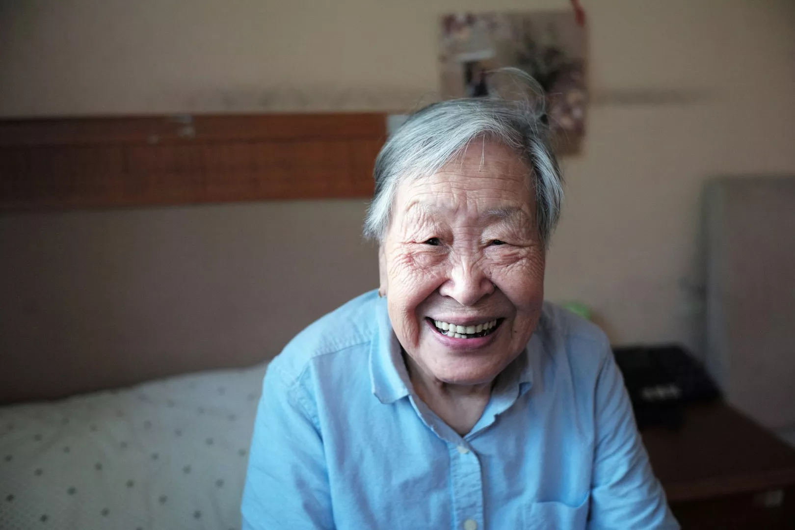 A caregiver wearing a yellow shirt is seated in front of a computer. She is showing an elderly client something on the screen. He is wearing a blue sweater and gazing intently at screen.